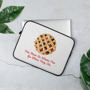 May include: White laptop sleeve with a black border. The sleeve features a colourful illustration of a pie with the text "This Must Be Where Pies Go When They Die" in red.