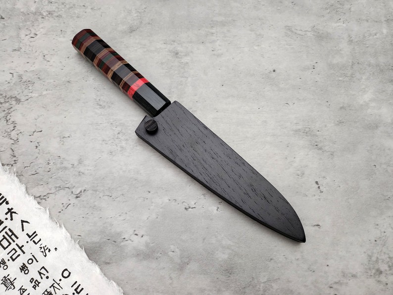 Puede incluir: Un cuchillo de cocina de madera negra con mango de madera roja, negra y marr&oacute;n.