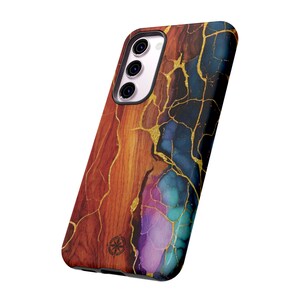Puede incluir: Una funda para smartphone con un dise&ntilde;o &uacute;nico. La funda presenta un patr&oacute;n de vetas de madera en tonos rojos, naranjas y marrones, con vetas doradas. El lado derecho de la funda tiene un dise&ntilde;o de m&aacute;rmol azul y morado. La funda tiene un recorte para la c&aacute;mara.