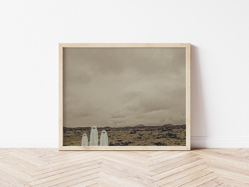 May include: A framed print of a landscape with three white ghosts standing in a field. The sky is cloudy and the field is a muted green color.