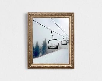 May include: A framed photograph of a ski lift with several empty chairs ascending a snowy mountainside. The lift is surrounded by a thick fog, creating a mysterious and atmospheric scene.