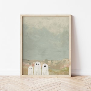 Peut inclure: Une peinture encadr&eacute;e repr&eacute;sentant trois fant&ocirc;mes blancs aux yeux noirs debout devant un paysage avec une cha&icirc;ne de montagnes en arri&egrave;re-plan. Le ciel est bleu clair avec des nuages.