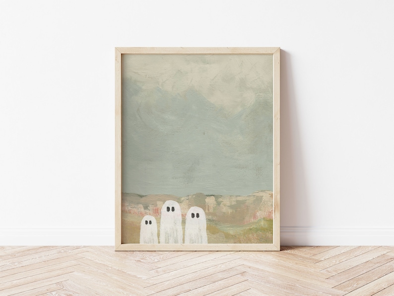Peut inclure: Une peinture encadr&eacute;e repr&eacute;sentant trois fant&ocirc;mes blancs aux yeux noirs debout devant un paysage avec une cha&icirc;ne de montagnes en arri&egrave;re-plan. Le ciel est bleu clair avec des nuages.