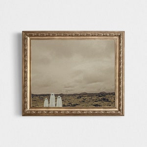 May include: A framed print of a sepia-toned landscape with three white ghost figures standing in a row in the foreground.