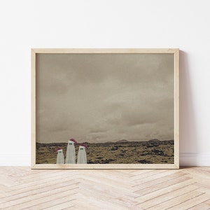 May include: A framed print of a landscape with three white ghosts wearing red Santa hats. The ghosts are standing in a field of brown grass with a cloudy sky in the background.
