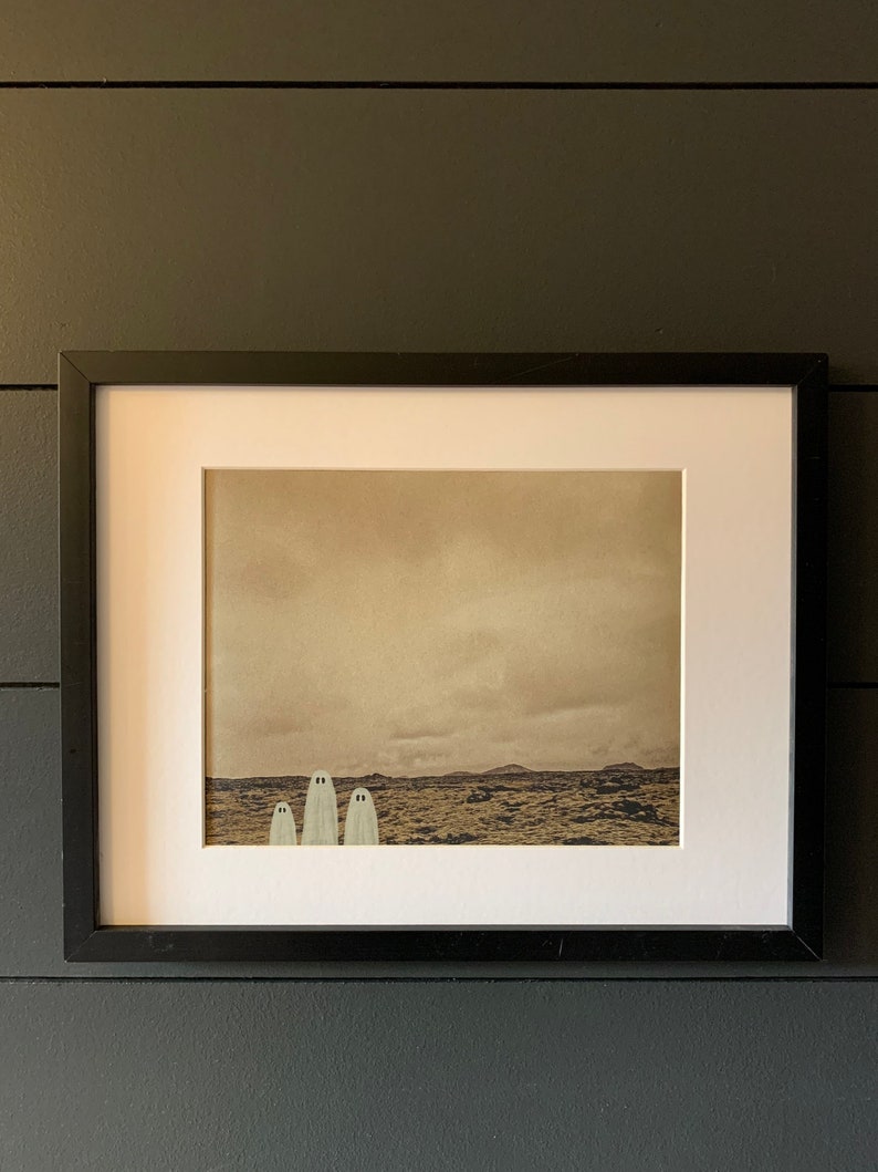 May include: A framed print of a sepia-toned landscape with three white ghosts standing in a row in the foreground.