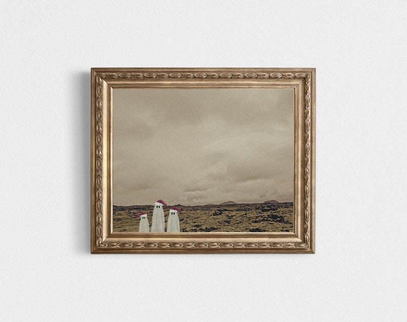 May include: A framed photograph of three white ghosts wearing red hats standing in a desolate landscape. The photo is in a gold frame with ornate detailing.