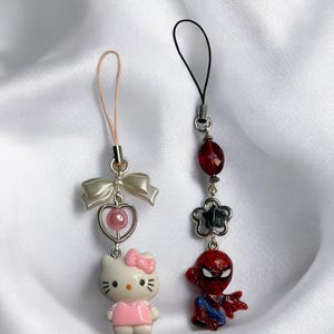 May include: Two phone charms, one with a pink Hello Kitty character and the other with a red Spiderman character.