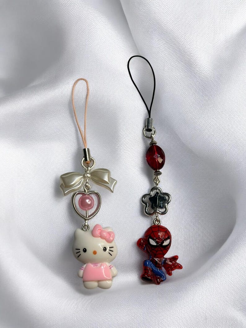 May include: Two phone charms, one with a pink Hello Kitty character and the other with a red Spiderman character.