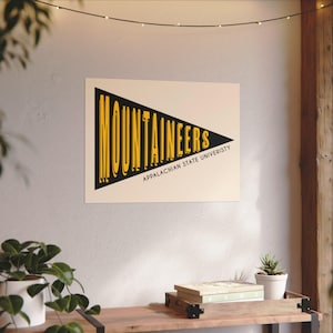 Könnte beinhalten: Ein schwarz-gelbes Banner mit dem Text "MOUNTAINEERS" und "APPALACHIAN STATE UNIVERSITY" in einer fetten, serifenlosen Schrift.