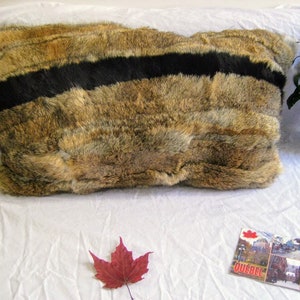 Peut inclure: Un oreiller en fausse fourrure marron et noir avec une bande noire au centre. L'oreiller est posé sur une surface blanche avec une feuille d'érable rouge et une carte postale.