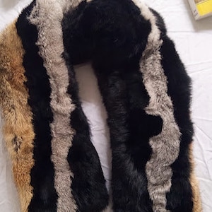 May include: A striped faux fur scarf in black, brown, and grey. The scarf is folded in a loop shape.