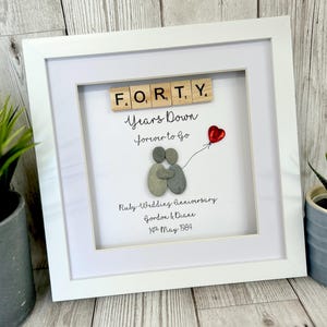 Può includere: Un'immagine incorniciata bianca con un design di arte di ciottoli che rappresenta una coppia che si abbraccia. L'immagine dice "Forty Years Down Forever to Go" e "Anniversario di matrimonio di rubino Gordon & Diane 14 maggio 1984".