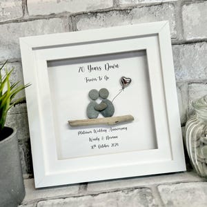 Può includere: Un'immagine incorniciata bianca con un design di arte di ciottoli che rappresenta una coppia che si tiene per mano. Il testo recita "70 Years Down Forever to Go Platinum Wedding Anniversary Wendy & Norman 30th October 2029".
