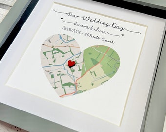 May include: A white framed print with a map of a town in the shape of a heart. The map is decorated with a red wooden heart. The print includes the text "Our Wedding Day Laura & Iain 26/06/2024 - St Neots Church."