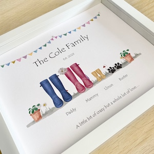 Peut inclure: Une impression encadrée blanche avec une illustration aquarelle d'une famille de quatre personnes et d'un chien. L'illustration présente des bottes de pluie colorées, des fleurs et une guirlande de drapeaux. Le texte "The Cole Family Est. 2023" est en haut de l'impression. Le texte "A little bit of crazy but a whole lot of love..." est en bas de l'impression.