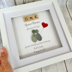 Pode incluir: Uma imagem emoldurada branca com um design de arte de seixos que representa um casal se abraçando. A imagem inclui as palavras "ONE Year Down forever to go" e "first Wedding Anniversary Rob & Jody 1st April 2023".