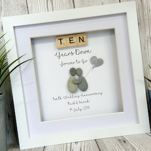 Pode incluir: Uma imagem emoldurada branca com um fundo branco. A imagem apresenta um casal feito de pedras cinzas segurando um balão de coração prateado. O texto "T. E, N Years Down forever to Go" está escrito em itálico preto. O texto "tenth Wedding Anniversary Rick & Sarah 21 July 2014" está escrito em itálico preto.