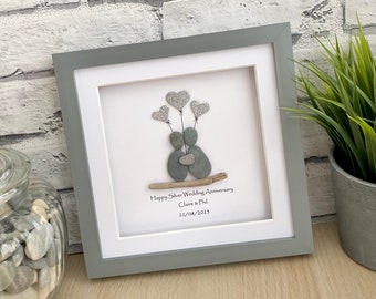 May include: A framed pebble art piece depicting a couple holding each other with silver glitter hearts floating above them. The text reads "Happy Silver Wedding Anniversary Claire & Phil 21/08/2023".