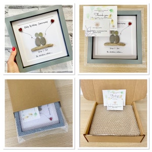 May include: A gray picture frame with a white mat and a pebble art design of two figures holding hands. The art is titled "Ruby Wedding Anniversary" and includes the text "George & Ann... The adventures continue..." The frame is packaged in a brown cardboard box with bubble wrap.