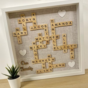 May include: A framed Scrabble tile word art piece with the words "Our Family" in wooden letters below the tiles. The tiles spell out the names of family members, including Robynn, Jacob, Amanda, Gary, Matthew, Mikey, Lauren, Ellie, and Flynn.