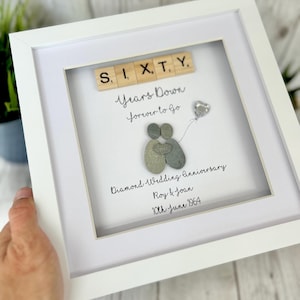 Può includere: Un'immagine incorniciata bianca con una coppia di pietre che tiene un palloncino a forma di cuore. L'immagine dice "Sessanta anni giù Per sempre andare" e "Anniversario di matrimonio di diamanti Roy & Joan 10 giugno 1964".