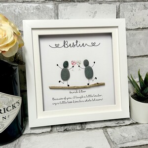 Puede incluir: Una imagen enmarcada en blanco con un fondo blanco. Dos figuras de guijarros grises sostienen copas de vino. El texto "Bestine" está escrito en la parte superior de la imagen. El texto "Sarah & Bev" está escrito debajo de las figuras. El texto "Because of you, I laugh a little louder, cry a little less & smile a whole lot more!" está escrito debajo de los nombres.