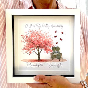 May include: A square white framed wall art piece featuring a printed pink cherry blossom tree, a brown bench, and two pebble figures sitting together. Red butterfly accents, the text On Your Ruby Wedding Anniversary, 1st December 1986, and Sue & Allan.