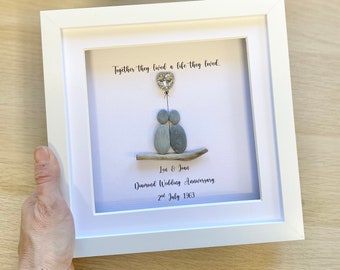 May include: A framed pebble art piece depicting a couple holding hands with a heart-shaped balloon above them. The text reads "Together they lived a life they loved. Len & Joan Diamond Wedding Anniversary. 2nd July 1963."