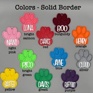 May include: A selection of brightly coloured paw-shaped pet tags. The tags are in shades such as light pink, bright salmon, red, burgundy, orange, blue, silver, yellow, green, and purple, each with a name printed on it.