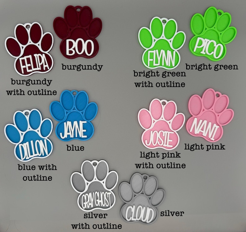 May include: A selection of paw-shaped pet tags in shades of burgundy, blue, green, pink, and silver. Each tag features a name, such as "FELIPA", "BOO", "FLYNN", "PICO", "DILLON", "JAYNE", "JOSIE", "NANI", "GRAY GHOST", and "CLOUD", with a contrasting outline.