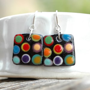 May include: A pair of black square earrings with colorful polka dots. The earrings are made of ceramic and have silver hooks.