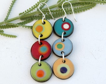 May include: A pair of dangle earrings with four colorful ceramic circles on each earring. The circles are decorated with different colored dots and circles. The earrings are silver.