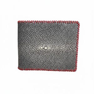 Peut inclure: Un portefeuille pliable doté d'un extérieur en peau de raie texturée noire et blanche, avec un groupe central proéminent de perles blanches plus grandes. Les bords du portefeuille sont finis avec un détail de surjet rouge épais et décoratif.