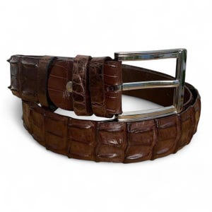 Op de afbeelding: Een bruine leren riem met een getextureerd krokodillenpatroon. De riem heeft een zilverkleurige rechthoekige gesp. De riem is ongeveer 3,8 cm breed.