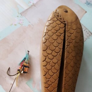 Pode incluir: Um quebra-nozes de madeira em forma de peixe, com um design esculpido de escamas. O quebra-nozes está aberto e pronto para quebrar nozes.
