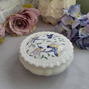 Könnte beinhalten: Eine weiße Keramik-Schmuckdose mit einem floralen Design in Blautönen, Gelb, Grün und Lila. Der Deckel hat einen gewellten Rand.