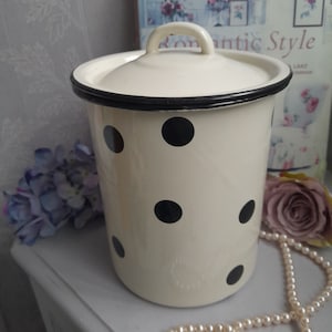 Peut inclure: Une boîte en émail blanc avec un couvercle noir et des pois noirs. La boîte a une poignée sur le couvercle.