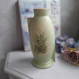 May include: A green ceramic vase with a floral design. The vase has a textured surface and a unique shape.