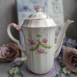 May include: White ceramic coffee pot with a pink floral design and a red lid. The pot has a fluted body and a delicate floral pattern.