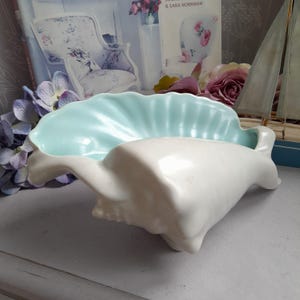 Op de afbeelding: Een witte keramische schelpvormige schaal met een lichtblauwe binnenkant. De schaal is gevormd als een schelp en heeft een gladde, glanzende afwerking.