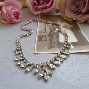 May include: A silver necklace with a teardrop-shaped crystal pendant. The necklace is made of small, clear crystals and has a delicate, vintage look.