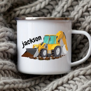 May include: White enamel mug featuring a yellow and black cartoon excavator with the name "jackson" in black script. The excavator is scooping up brown dirt. The mug has a silver rim and a white handle.