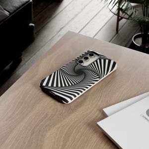 May include: A rectangular smartphone case featuring a high-contrast black and white optical illusion pattern of radiating, swirling lines that converge toward the center. The case has a cutout for a triple-lens camera system on the back.