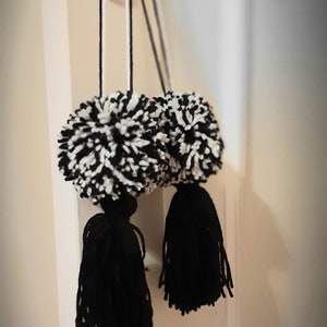 May include: Two black and white pom-poms with black tassels hanging from a door handle.
