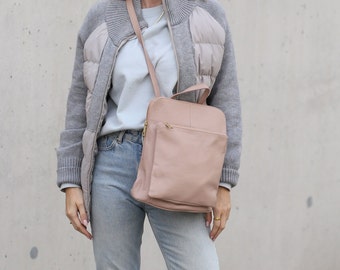 May include: A woman wearing a gray and white puffer jacket with a light blue shirt and light blue jeans. She is carrying a light pink leather backpack.