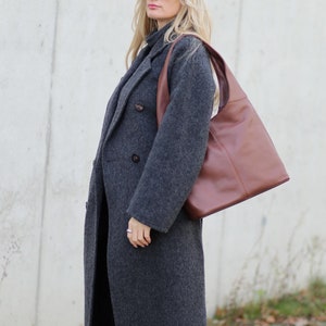 May include: A woman wearing a grey wool coat, black jeans, brown suede ankle boots, and sunglasses. She is carrying a brown leather tote bag.