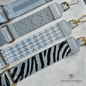 Könnte beinhalten: Vier verschiedene blaue und weiße gemusterte Riemen mit goldener Hardware. Die Riemen sind aus Stoff und Leder. Die Riemen sind für Taschen oder Handtaschen.