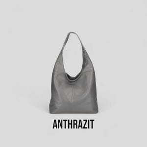 May include: A grey leather hobo bag with a slouchy design. The bag has a single strap and a large opening.