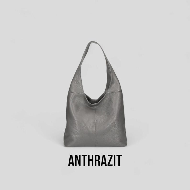 May include: A grey leather hobo bag with a slouchy design. The bag has a single strap and a large opening.